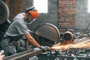 Side ,,view, cutting the metal. Young factory worker in grey uniform photo