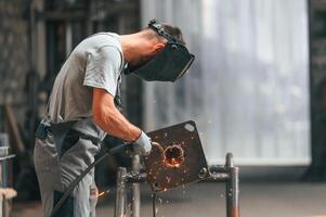 Process, of welding. Young factory worker in grey uniform photo