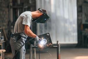 Process ,of welding. Young factory worker in grey uniform photo