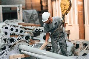 Using, crane hook. Young factory worker in grey uniform photo