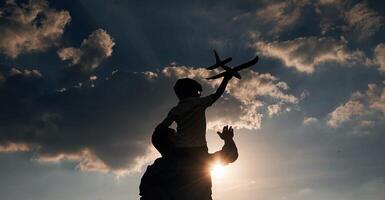 Against dramatic sky, with toy plane, sitting on shoulders. Father and little son are playing and having fun outdoors photo