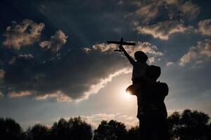 Against ,dramatic sky, with, toy, plane, sitting on shoulders. Father and little son are playing and having fun outdoors photo