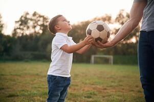 Boy, is taking soccet ball. Father, and little son are playing and having fun outdoors photo