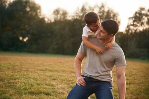 Embracing ,dad from ,behind. Father and little son are playing and having fun outdoors photo