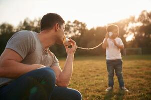 Talking, by using string, can phone. Father and little son are playing and having fun outdoors photo