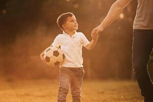 Illuminated by sunlight, holding soccer ball. Father and little son are playing and having fun outdoors photo