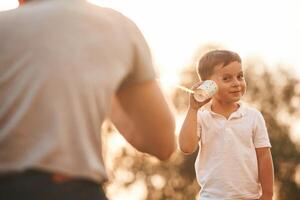Fun,,, holding and using string can phone. Father and little son are playing outdoors photo