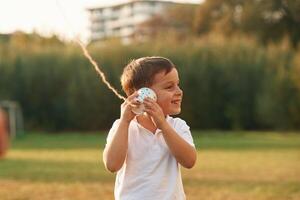 Using string can phone. Little boy is playing outdoors at daytime photo
