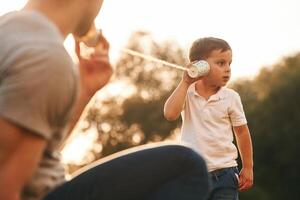 Fun,, holding and using string can phone. Father and little son are playing outdoors photo