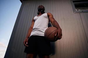Standing,, against metal surface building. Young black man is with basketball ball outdoors photo