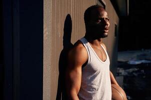 Standing, against metal surface, building. Young black man is with basketball ball outdoors photo