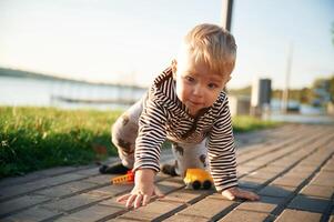 Crawls on, the cobblestones. Cute little boy is having fun outdoors on the ground with green grass photo