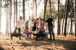 Doing cheers with bottles of beer. Group of friends are together ,in the forest photo