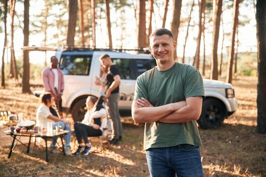 Man is standing with arms crossed and smiling. Group of friends are together in the forest photo