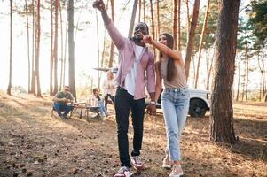Couple are holding each ,other, by the hands, walking. Group of friends are together in the forest photo