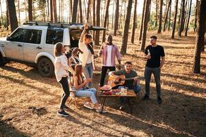 Drinking,, eating,,, playing with dog. Group of friends are together in the forest photo