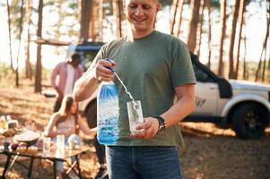 Man with fresh water. Group of, friends are together in the forest photo