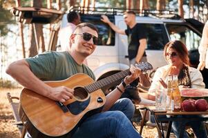 Musician, playing g,uitar. Group of friends are together in the forest photo