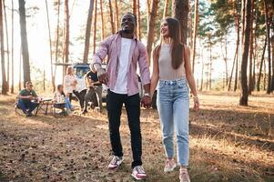 Couple are holding each other ,by ,the hands, walking. Group of friends are together in the forest photo