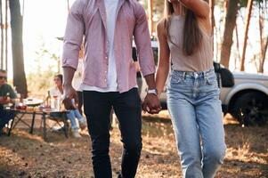 Close up view of couple that holding each other by hands. Group of friends are together in the forest photo