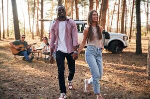 Couple are, holding, each other by the hands, walking. Group of friends are together in the forest photo