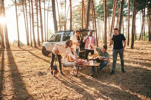 Drinking, eating,,, playing with dog. Group of friends are together in the forest photo