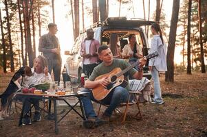 Acoustic guitar, player. Group of friends are together in the forest photo