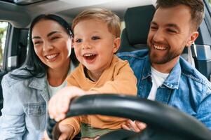 Boy, is trying to ride. Family of father, mother and little son are sitting in the modern car photo