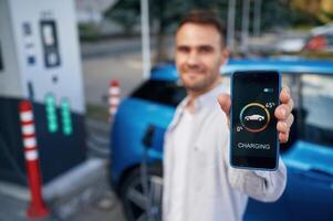 Showing process on the display of smartphone. Man with blue electric car on the, charge ,station photo