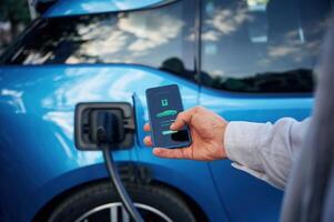 Showing, process ,on, the display of smartphone. Man with blue electric car on the charge station photo