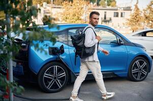 With ,backpack. Man, with ,blue electric car on the charge station photo