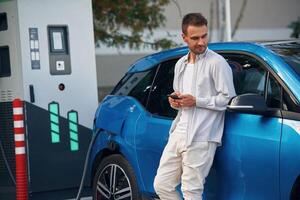 Standing and waiting for process finished.. Man with blue electric car on the charge station photo