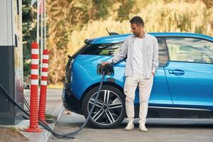 Front view., Man with blue electric car on the charge station photo