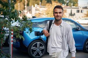 With ,backpack. Man with blue electric car on the charge station photo