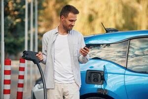 Front view. Man with, blue electric car on the charge station photo