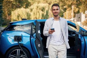 Front view. Man with blue electric, car, on the charge station photo