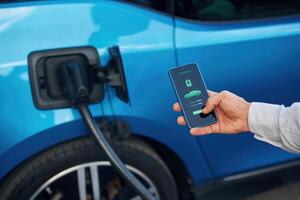 Charging process on, the ,display of smartphone. Man with blue electric car on the station photo