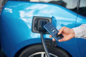 Charging process,, on the display of smartphone. Man with blue electric car on the station photo