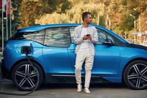 Blue, vehicle, holding, smartphone. Man with blue electric car on the charge station photo