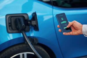 Charging process, on the display of smartphone. Man with blue electric car on the station photo