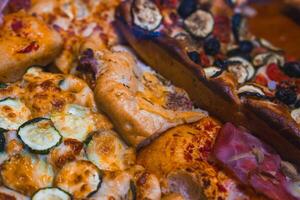 Freshly baked pizzas and focaccias with zucchini, eggplant, olives, ham, and cheese. Golden crusts and vibrant toppings in a Bergamo bakery setting. photo
