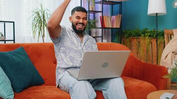 espantado indiano homem usar computador portátil computador, receber Boa notícia mensagem, chocado de vitória, comemoro ganhar video