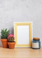 Empty photo frame with cacti, candle and copy space on wooden table