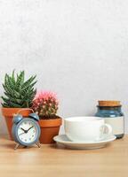 Coffee cup, alarm clock and cacti creating relaxing morning atmosphere on desk photo
