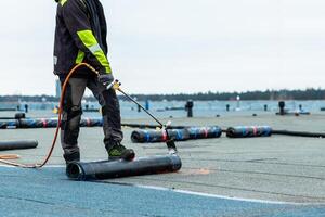 Worker Applies Torch On Roofing Material on Flat Rooftop Near Waterfront photo