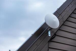 Circular White Wi Fi Router Mounted on Slanted Roof of Private House photo