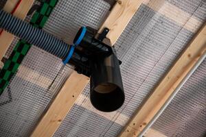 Section of a house under construction featuring a recuperation ventilation system with black and blue ducts on a wooden ceiling framework. photo