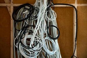 an Construction site interior showing coiled black and white conduits hanging on a wooden frame, with exposed studs and insulated walls in the background. photo