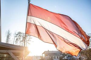 Latvian Flag Waving with Trees, Rooftops, and Wooden Structure photo