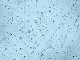 Clear water droplets scattered across a glass surface with a soft blue sky behind. photo